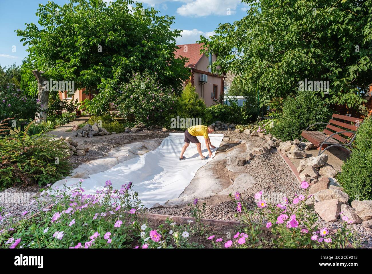 man roll out a roll of white non-woven geotextile fabric to set up fish pond Stock Photo