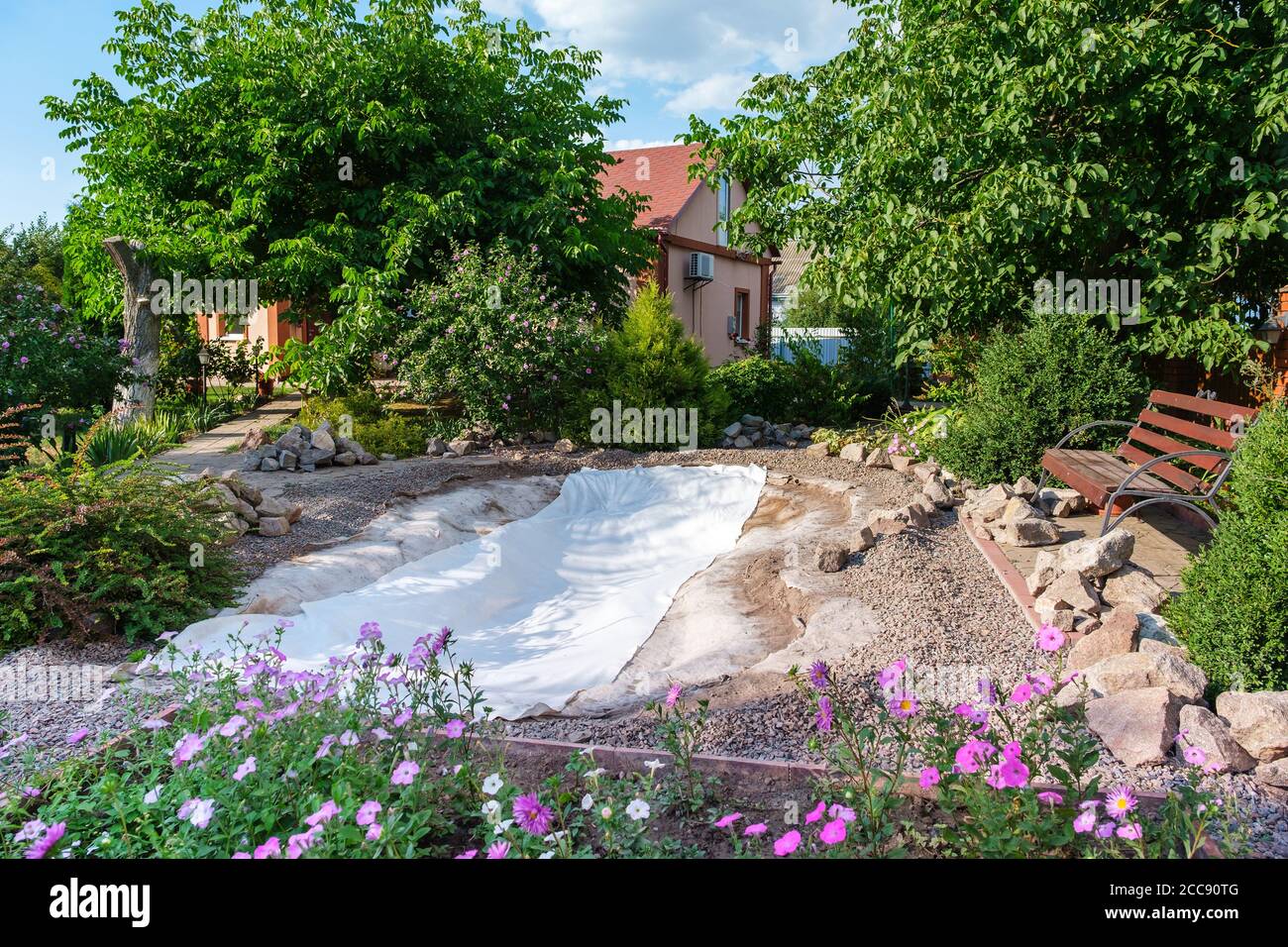 Family roll out a roll of white non-woven geotextile fabric to set up fish pond Stock Photo