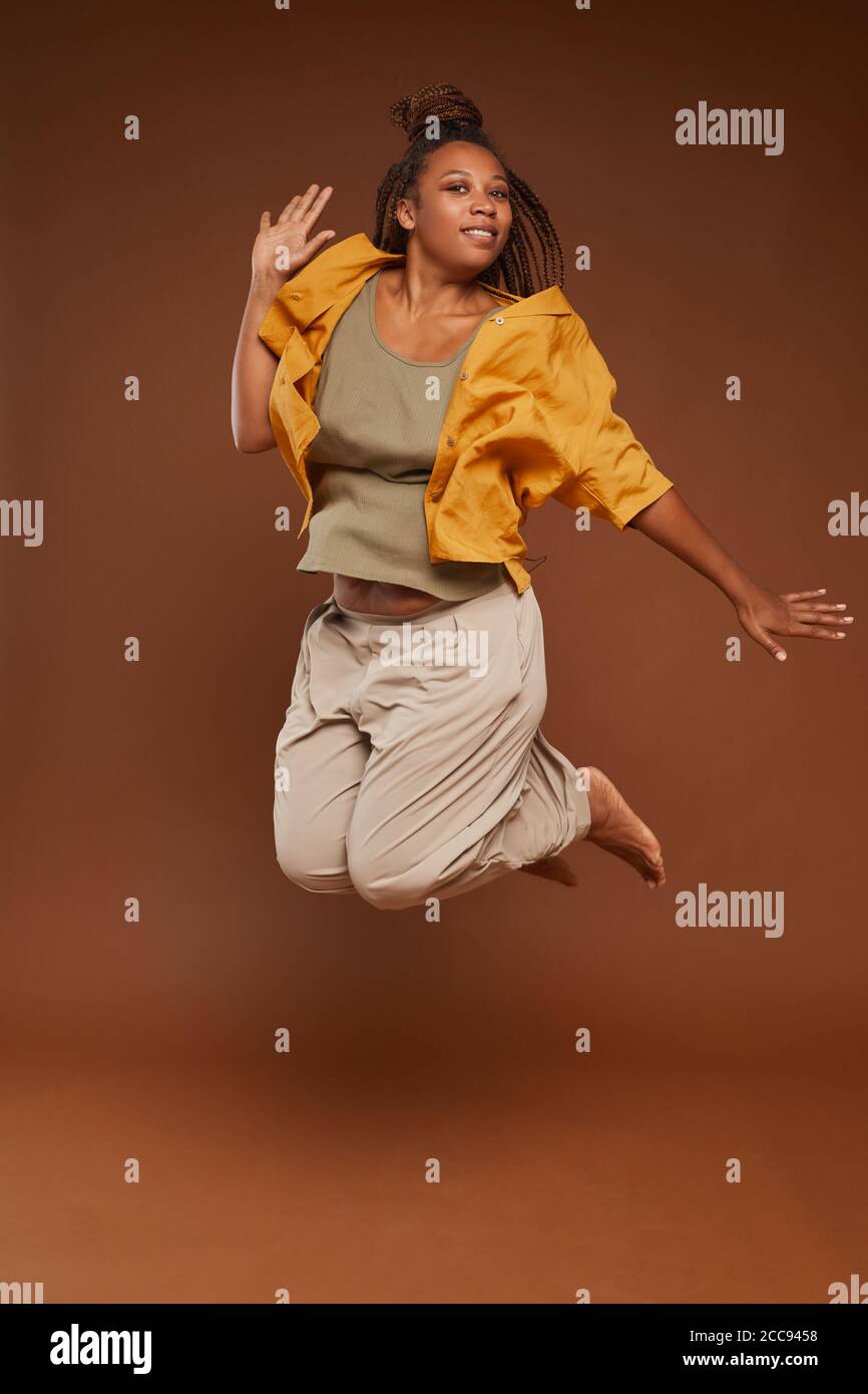 Portrait of African happy woman in fashion clothes jumping against the brown background Stock Photo