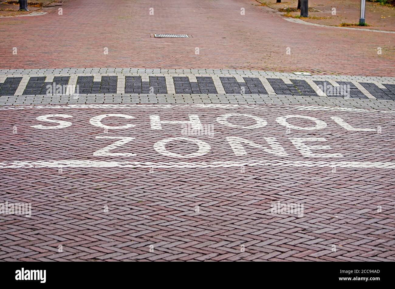 The words 'school zone' witten in white paint on a brick road in wolle, The Netherlands, to encourage drivers to reduce speed Stock Photo