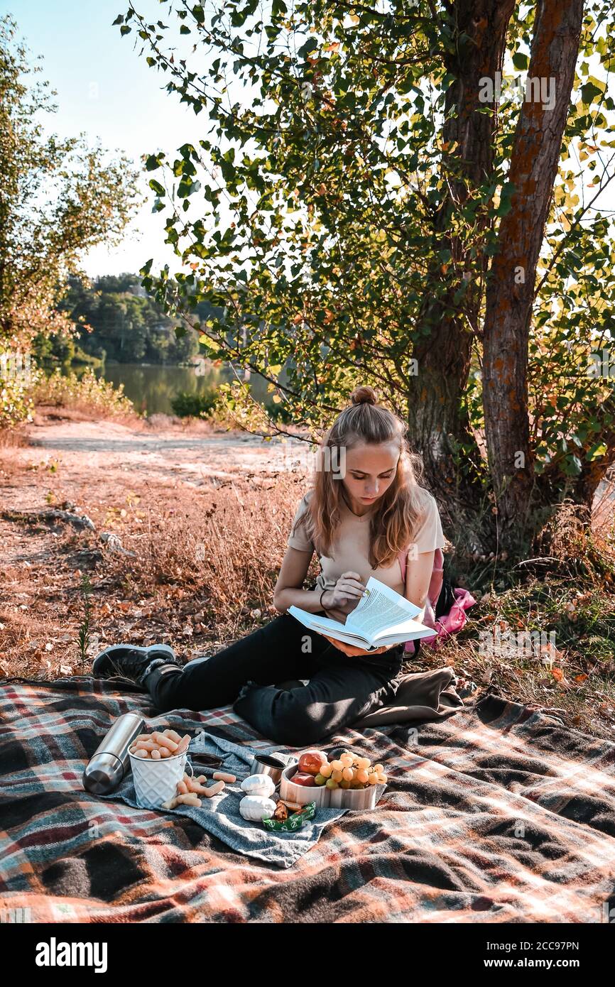 Young girl, student sitting outdoor with backpack and reading a book. Study from home. Cottagecore Stock Photo