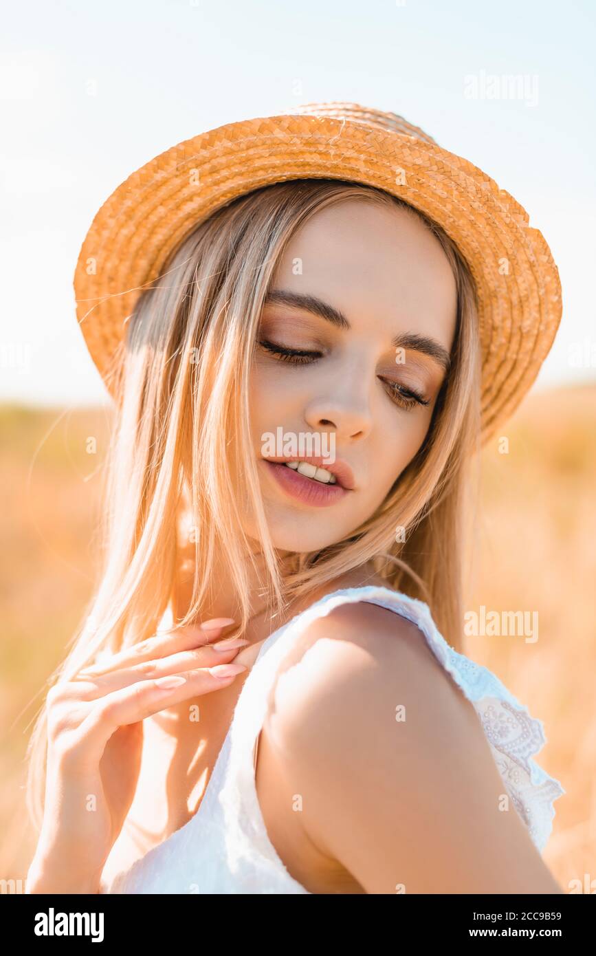sensual blonde woman in straw hat and summer outfit touching shoulder