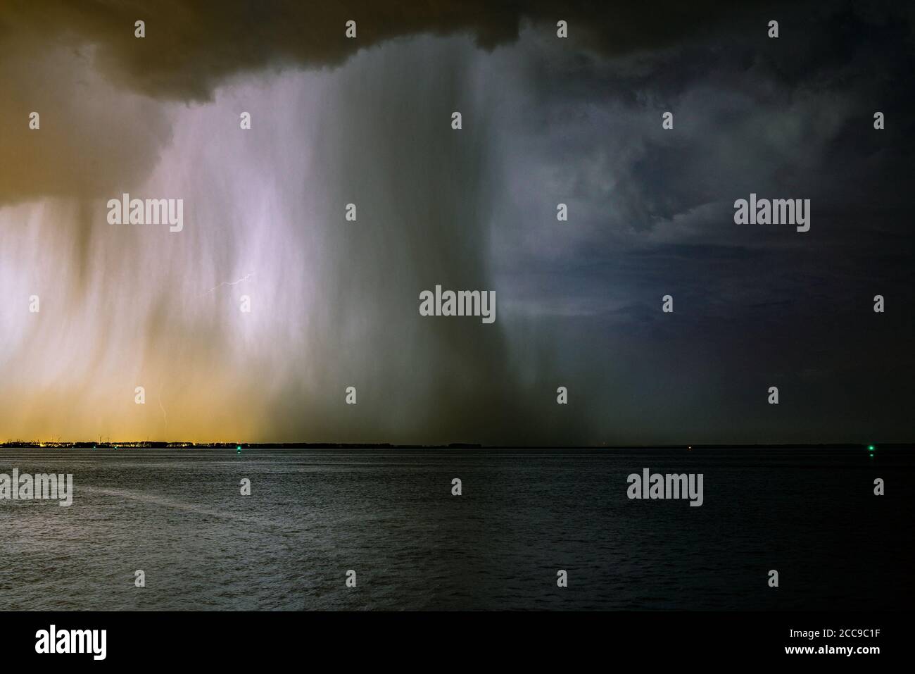 Dramatic nature image of a thunderstorm with distinct rain and hail shaft over a lake. Night time image. Stock Photo