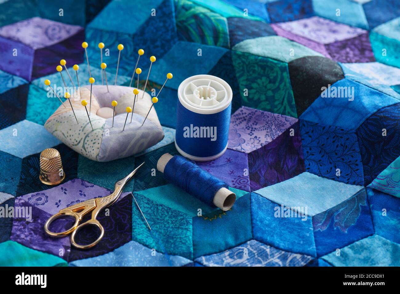 Pincushion, spools of thread, scissors and thimble on the tumbling blocks quilt background Stock Photo