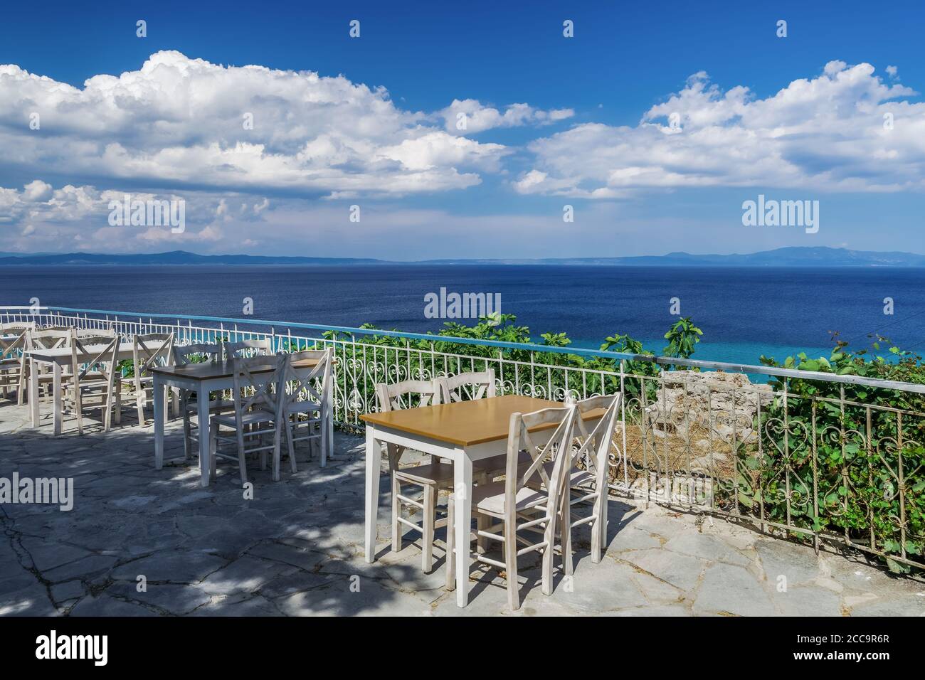 Chalkidiki, Greece empty tavern wooden chairs & table after new covid-19 measures. Restaurant outdoor seating area above the sea without customers. Stock Photo