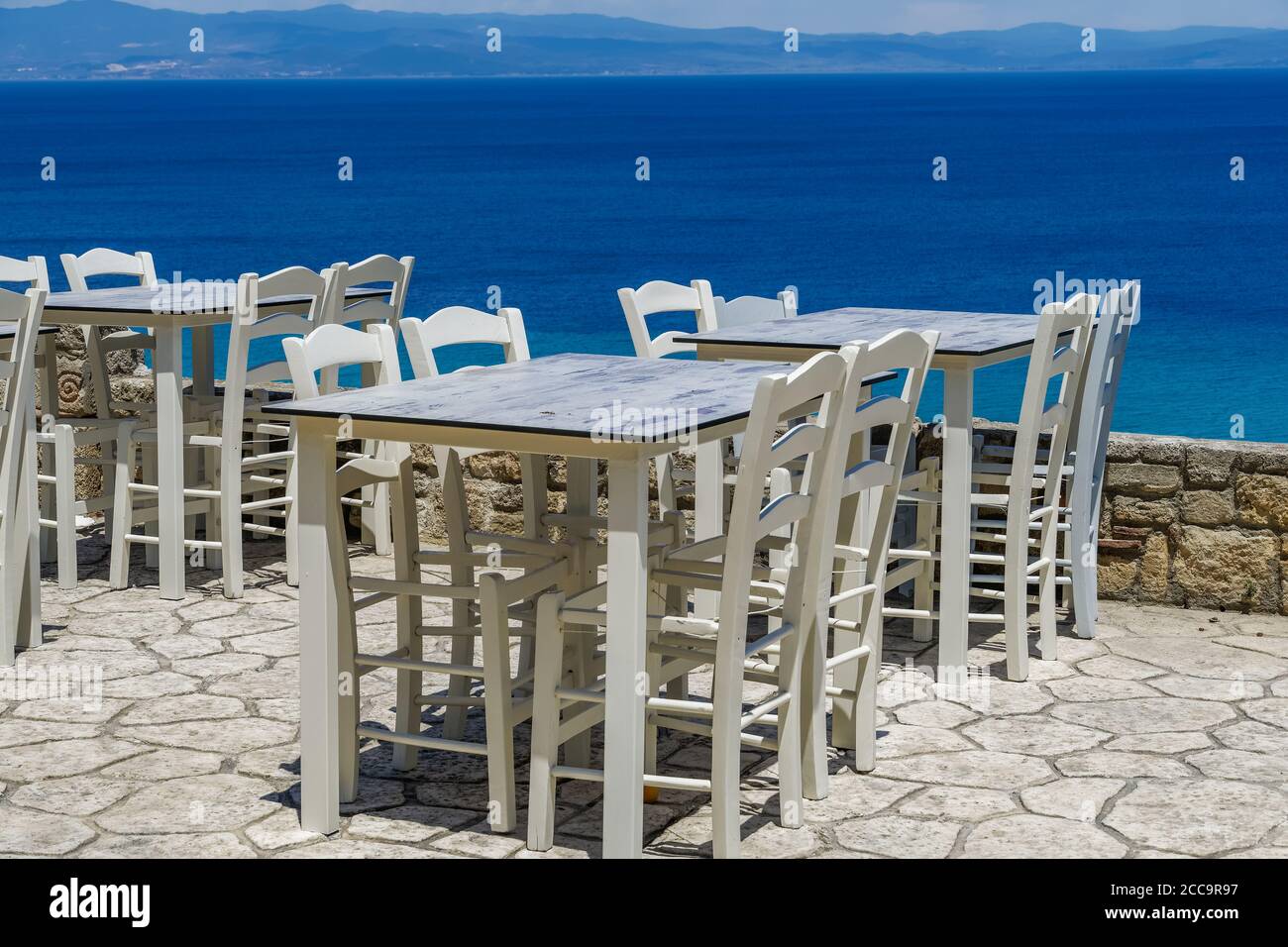 Chalkidiki, Greece empty tavern wooden chairs & tables after covid-19 measures. Sea view restaurant outdoor seating area without customers in Athytos. Stock Photo