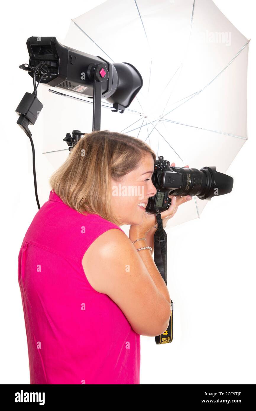 Vertical portrait of a photographer using a DSLR camera and a light to take photos in a studio. Stock Photo