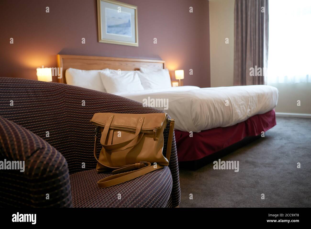 A photograph of a handbag on a chair in a hotel room. Stock Photo