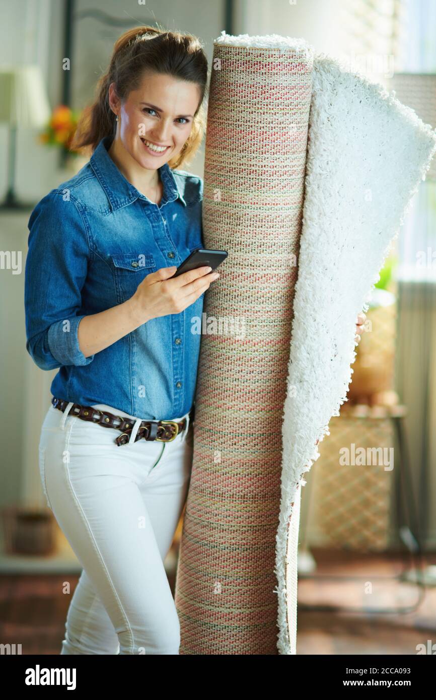 smiling young housewife in jeans shirt and white pants with white carpet  searching for carpet cleaning service on a smartphone in the modern living  ro Stock Photo - Alamy