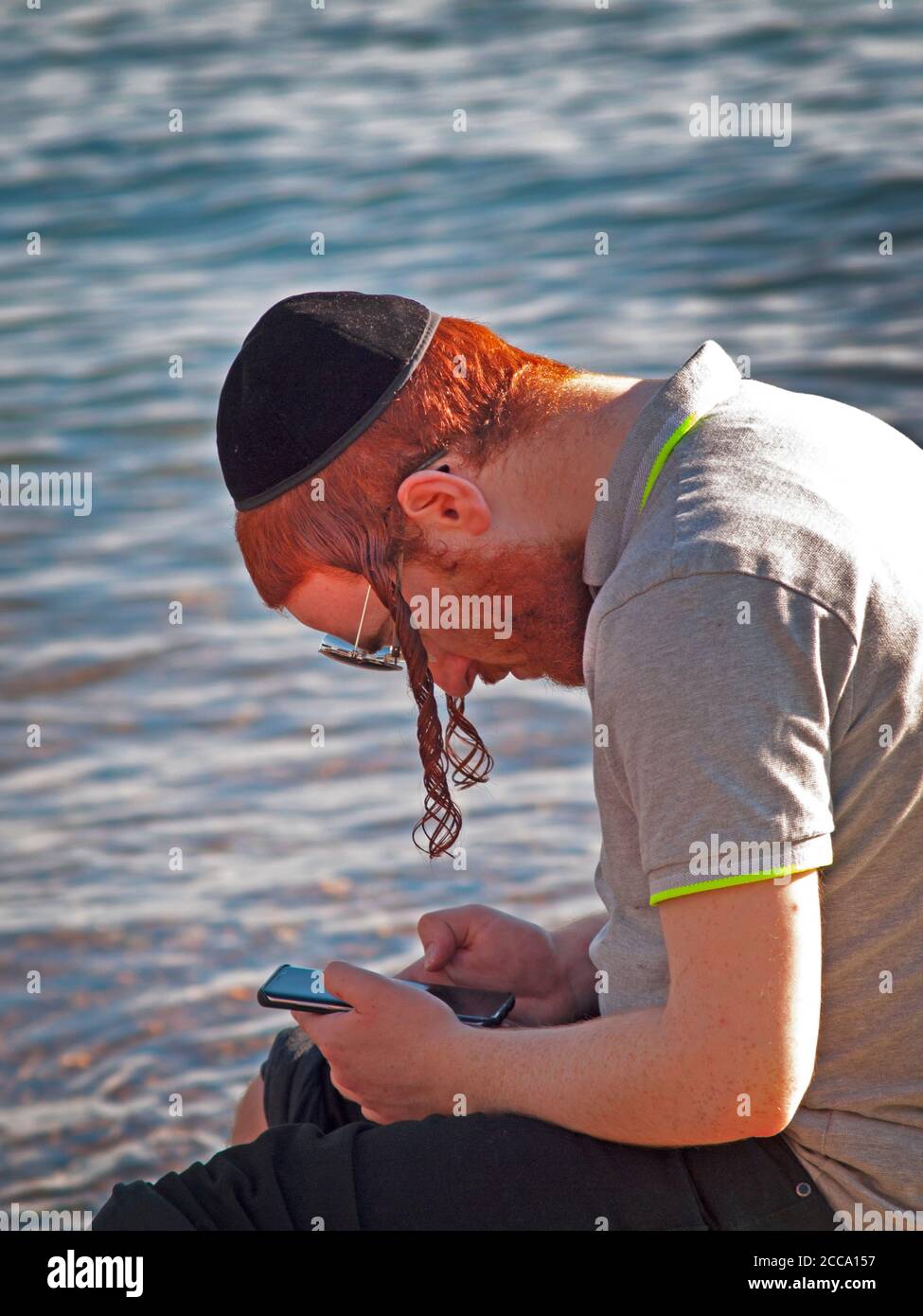 An Orthodox Jewish man checks his phone by the sea at Brighton, England Stock Photo
