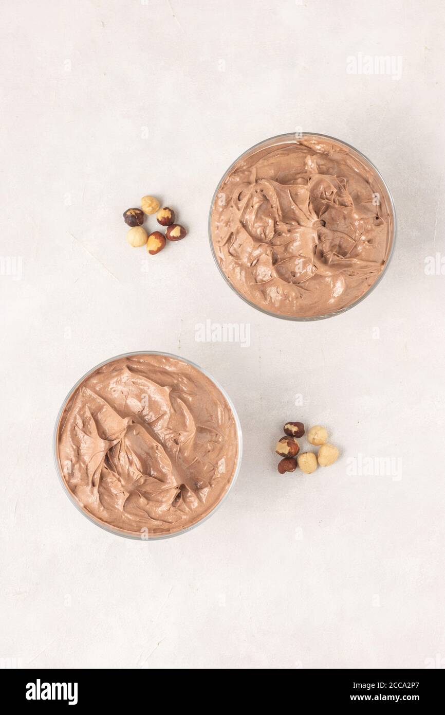 Tasty chocolate mousse dessert placed on white background with hazelnuts, top view, flat lay. Stock Photo