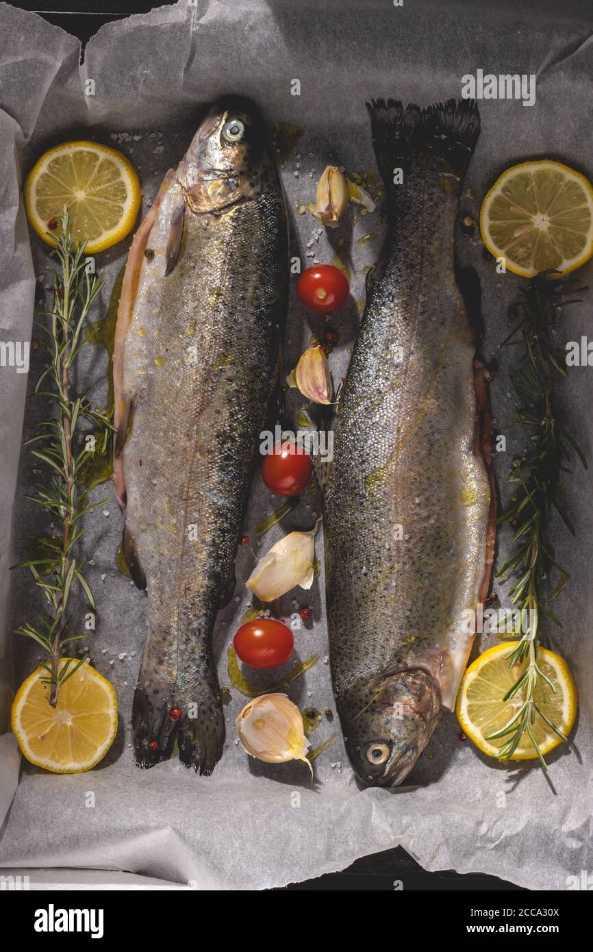 Fresh raw trout with olive oil, rosemary, cherry tomato, pepper, salt and lemon. Healthy Mediterranean food and dieting concept, top view, flat lay. Stock Photo