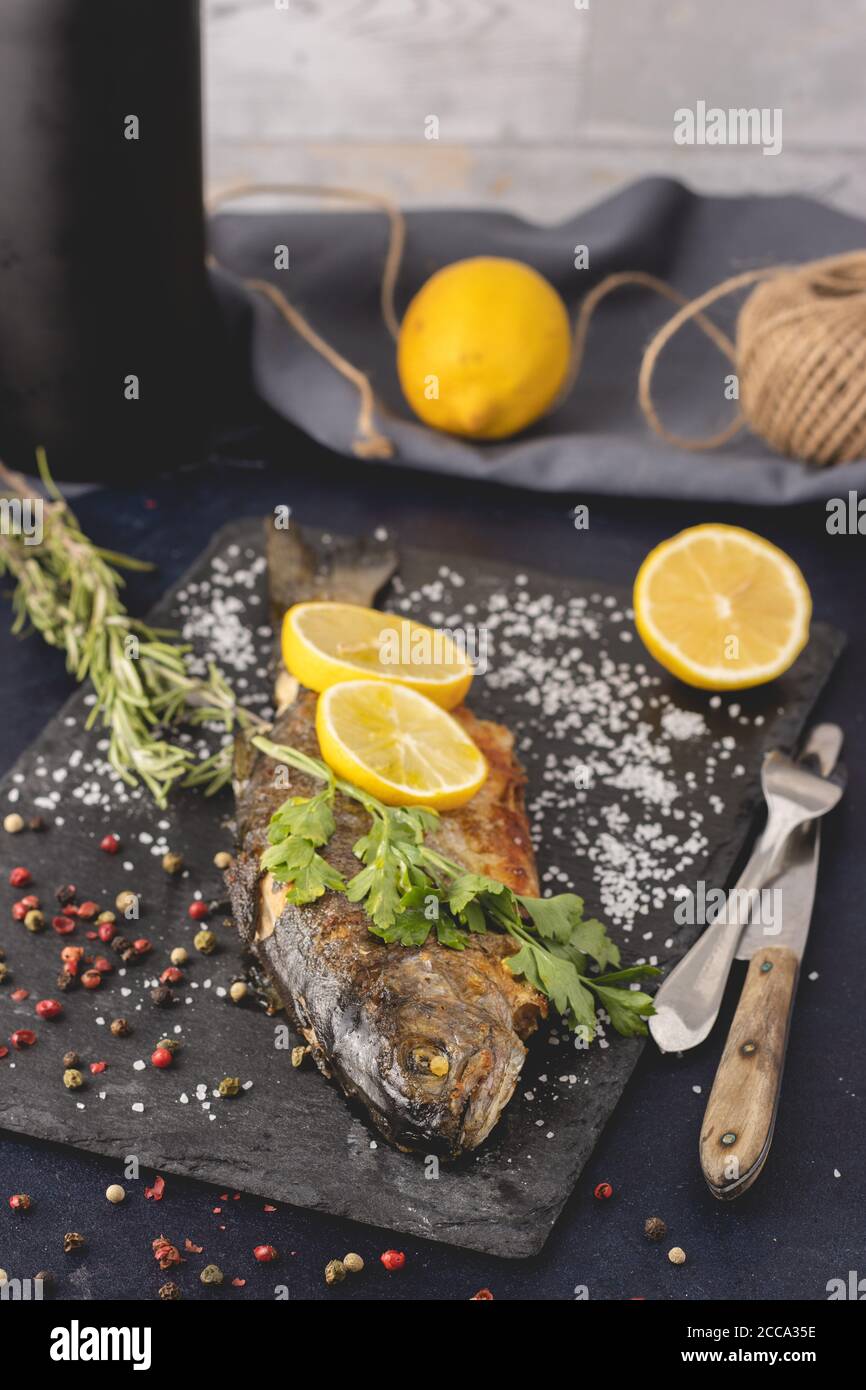 Grilled trout with olive oil, rosemary, pepper, salt and lemon placed on the dark background. Healthy Mediterranean food and dieting concept. Stock Photo