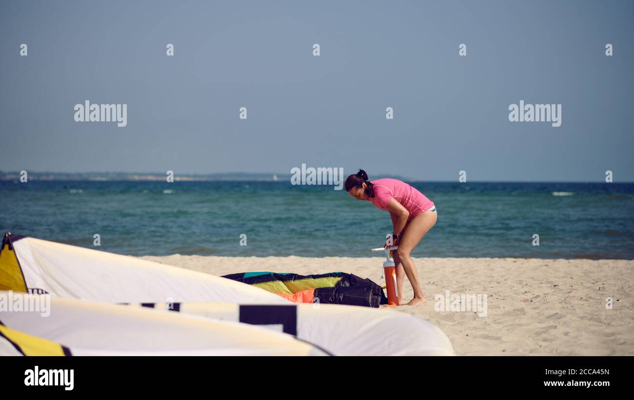 Middle-aged woman pumping up up a kitesurfing kite at the beach on summer vacation in hot sunshine with ocean backdrop Stock Photo