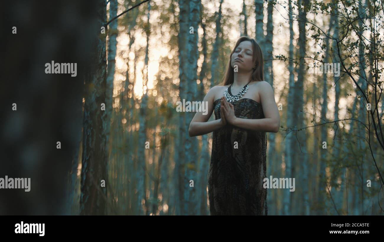 young woman praying with closed eyes in nature during the sunset ...