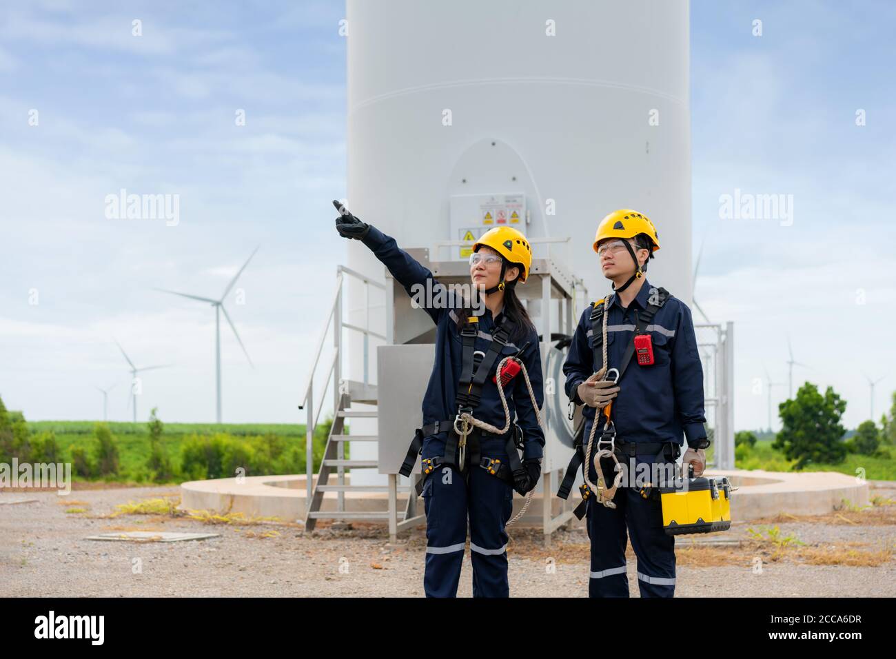 Asian man and woman Inspection engineers preparing and progress check of a wind turbine with safety in wind farm in Thailand. Stock Photo
