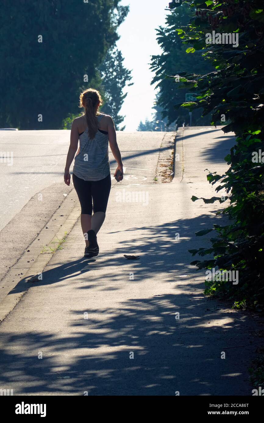 Silhouette of a young woman in running gear walking uphill holding a cell phone.  Stock photo. Stock Photo