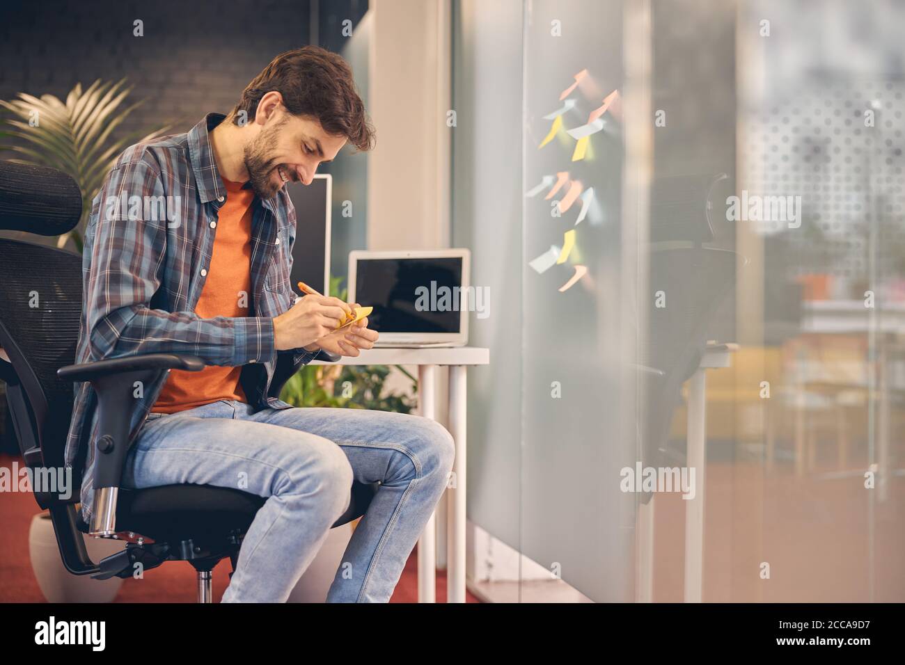 Cheerful young man writing on sticky notes at work Stock Photo - Alamy