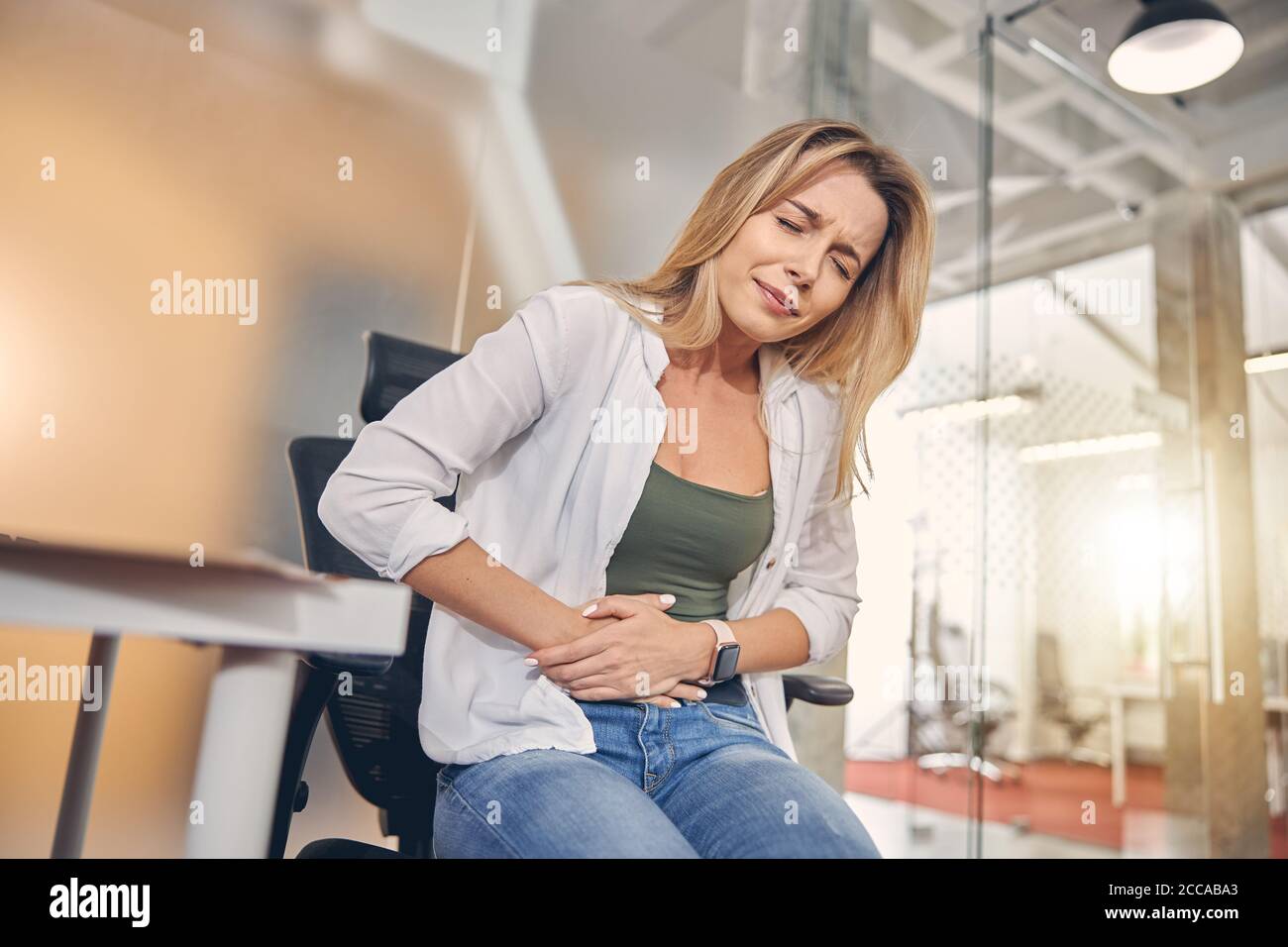 Upset young woman suffering from stomachache in office Stock Photo