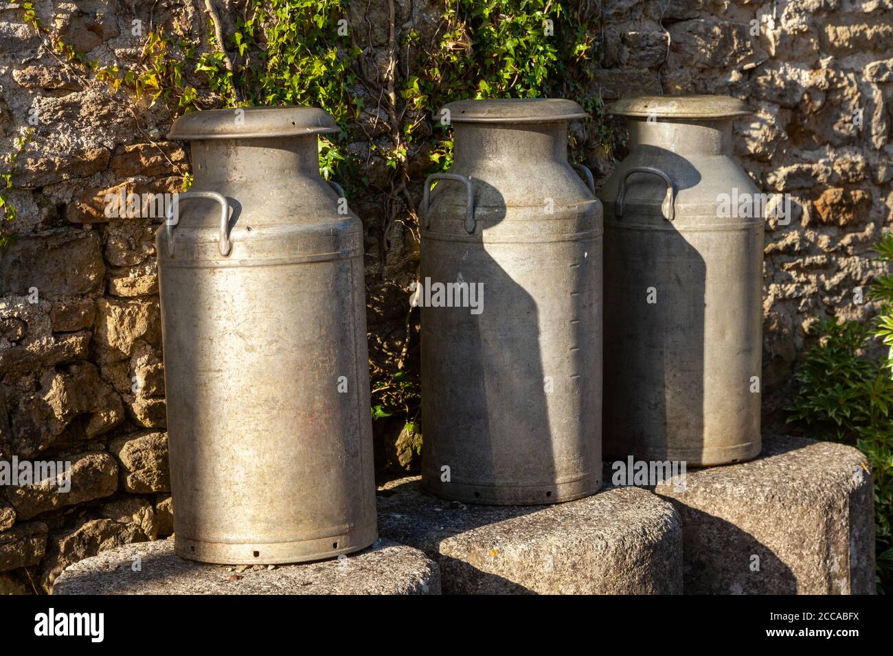 Three milk churns and stone wall as background Stock Photo