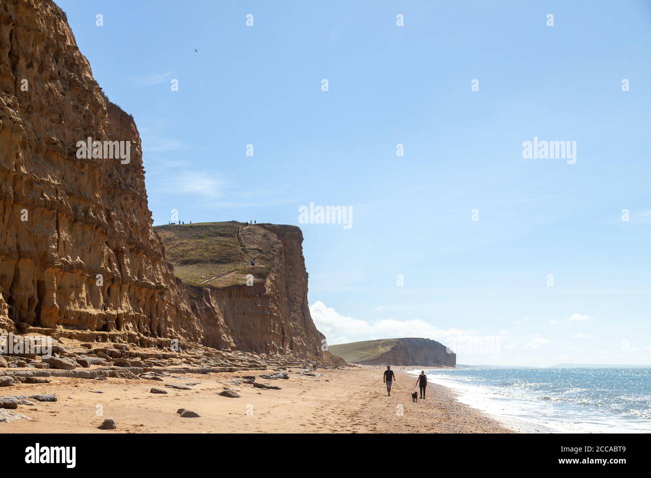 Two walkers walking under the dramatic cliffs near Burton Freshwater on the Jurassic Coast, Dorset, England, UK Stock Photo