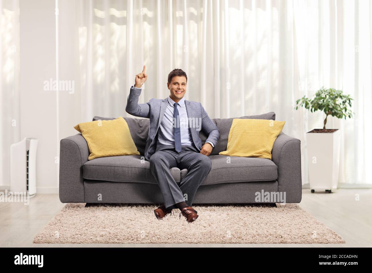 Man in elegant clothes sitting on a sofa at home and pointing up Stock Photo