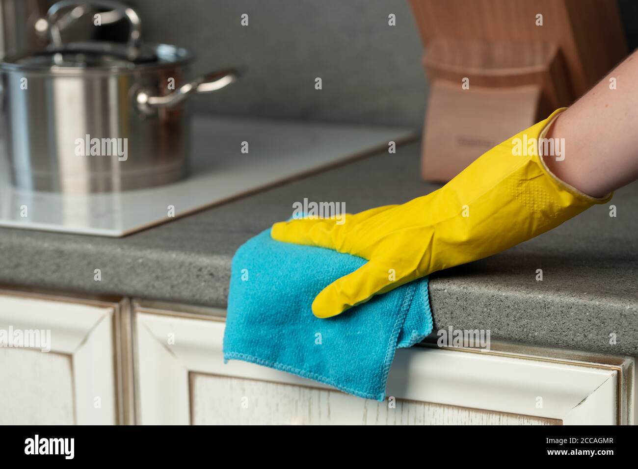 Woman's hands in yellow gloves cleaning counter top in kitchen Stock