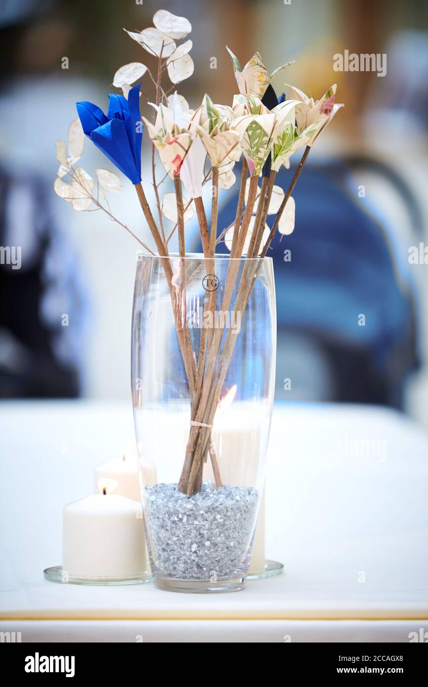 Stylish paper flowers in a glass being used as a table decoration at a wedding reception Stock Photo