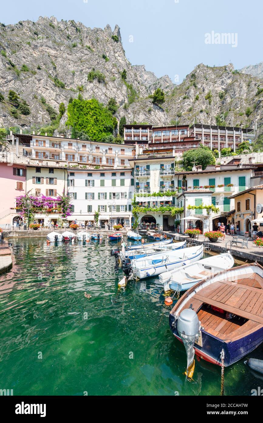 Boats in the old harbour of Limone in front of colorful facades below the cliffs and rock faces of the mountains on Lake Garda, Italy Stock Photo