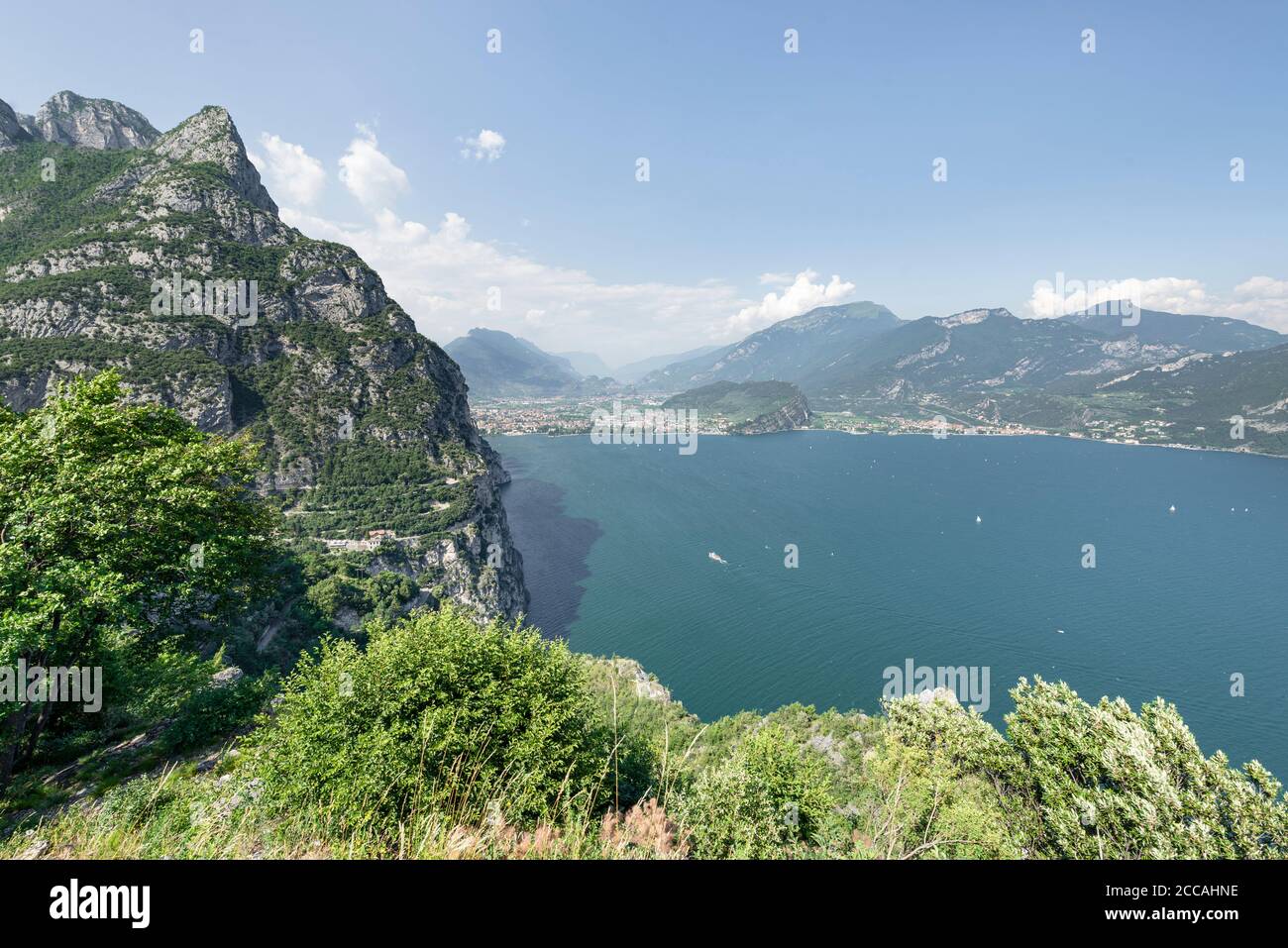 View of the serpentines of the old Ponale road and the rocky steep bluffs of Lake Garda with the panorama of Riva del Garda and the Alps , Italy Stock Photo