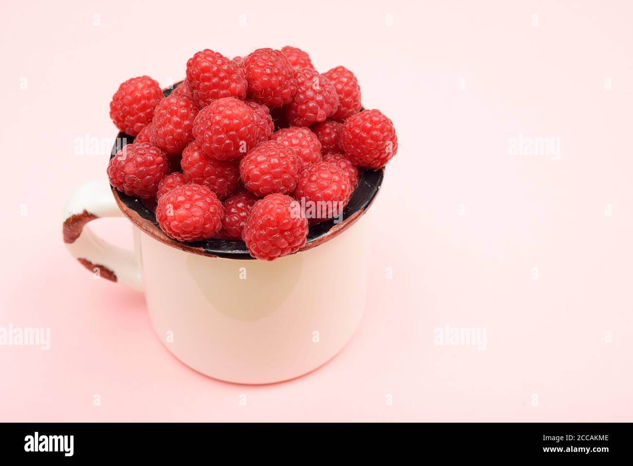 large ripe raspberries in a mug on a pink background Stock Photo