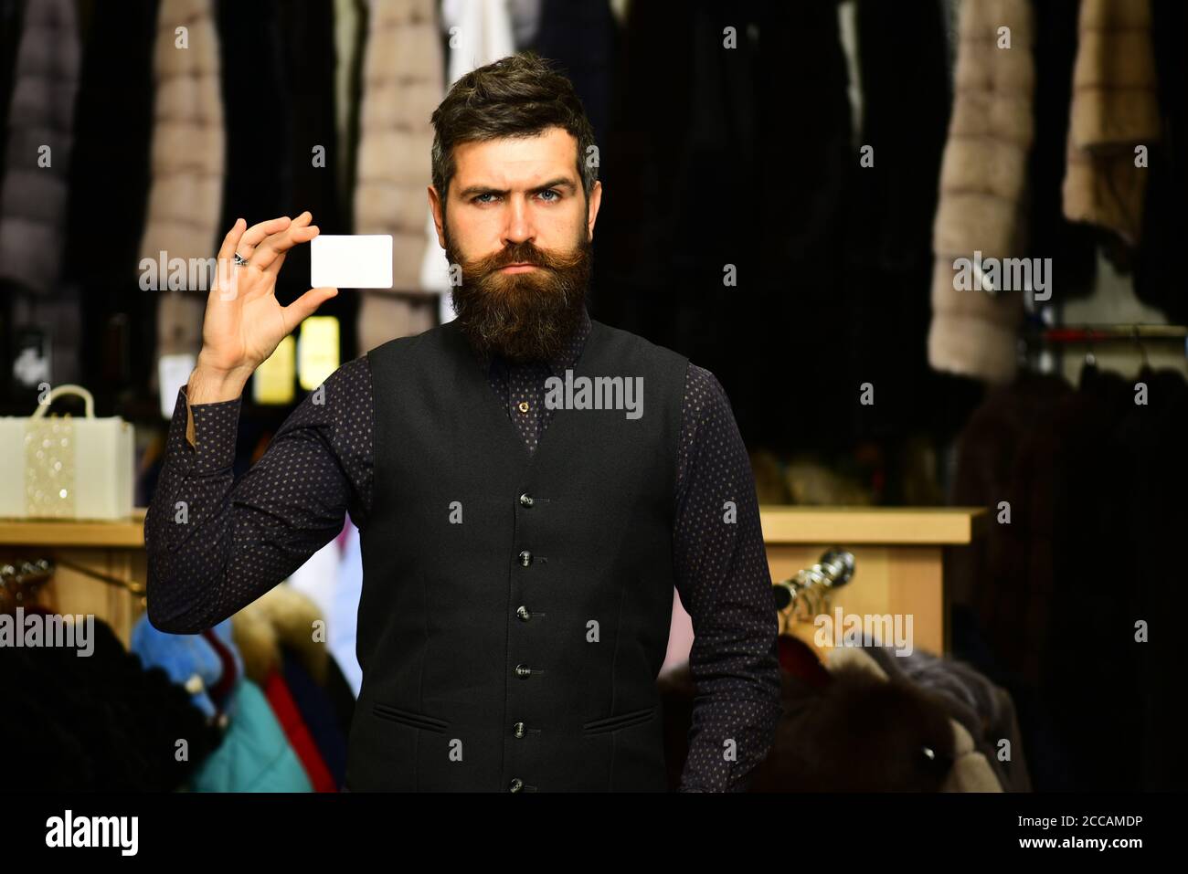 Customer with beard and business card. Shop assistant with empty paper.  Finance and shopping concept. Man with strict face holds card on furry  coats racks background, defocused Stock Photo - Alamy