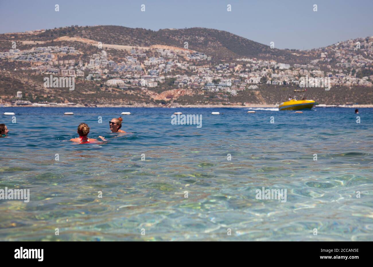 Young women ( model released ) swim at the Kalkan beach club with the town of Kalkan in the bacground. Kalkan is a popular holiday destination and is Stock Photo