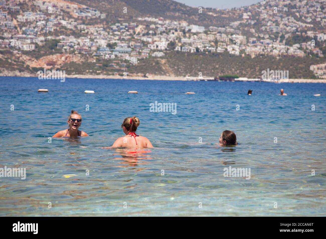 Young women ( model released ) in the sea at the Kalkan beach club with the town of Kalkan in the bacground. Kalkan is a popular holiday destination a Stock Photo