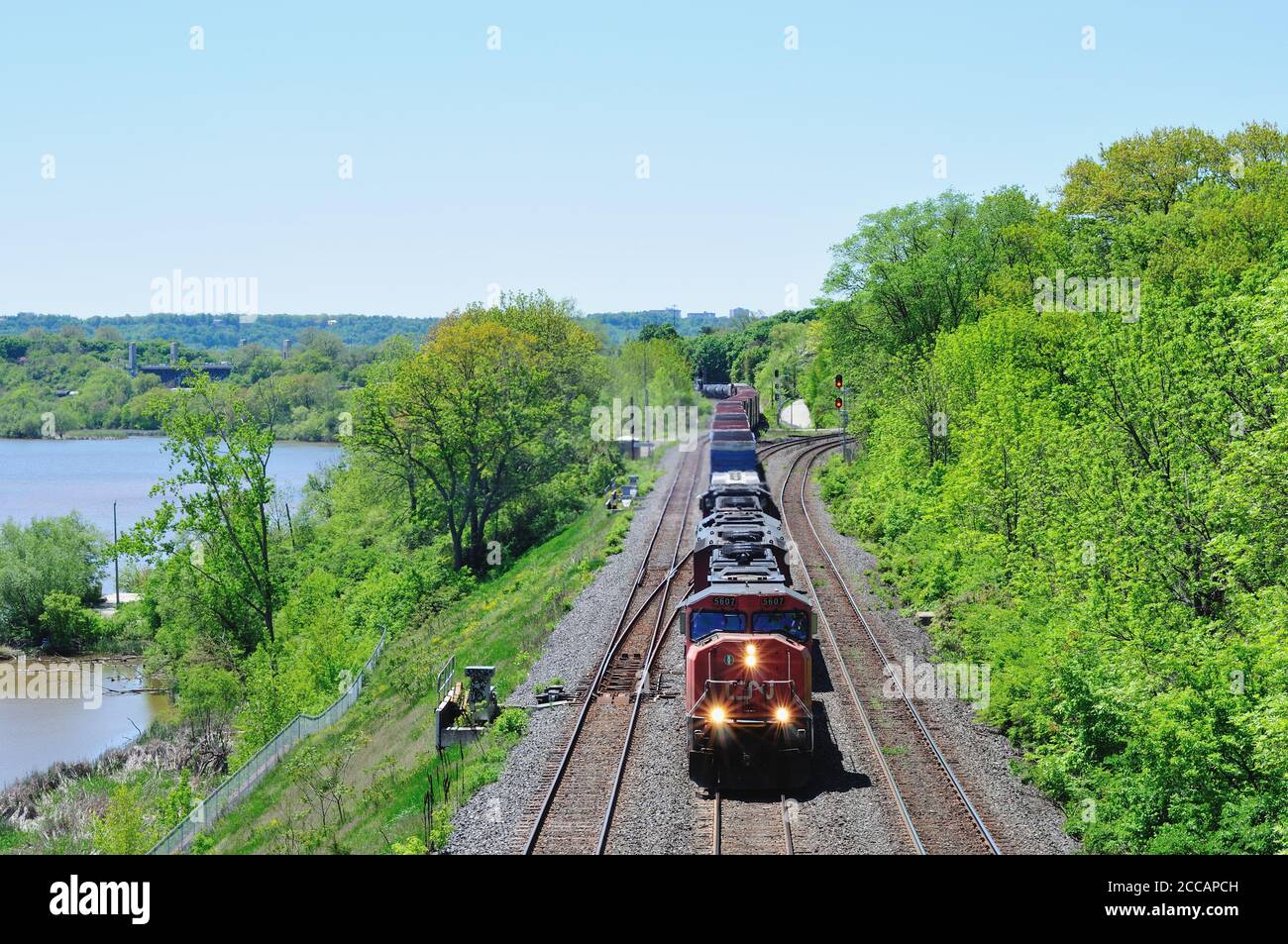 Oncoming CN freight train with lit headlights carrying containers, tanker cars and cargoes passing through Hamilton, Ontario, Canada during daytime Stock Photo