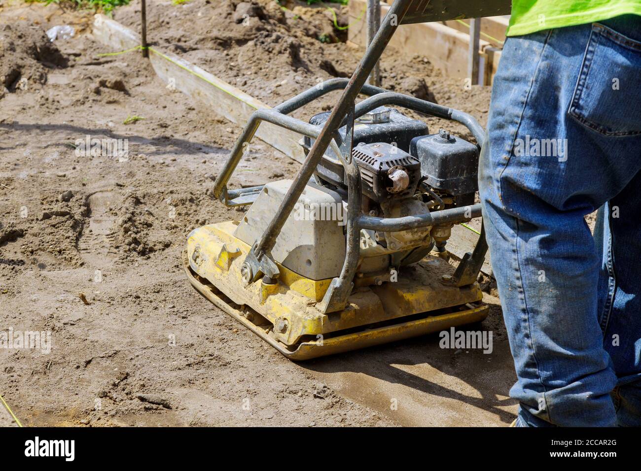 Worker uses compactor to vibratory hammer power tool at soil at