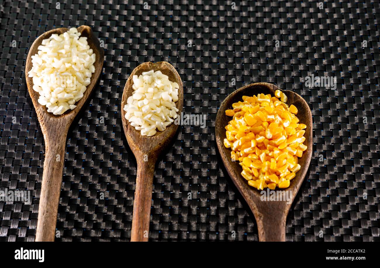 Corn seeds for hominy preparation. Hominy in yellow and white in wooden spoons. Brazilian