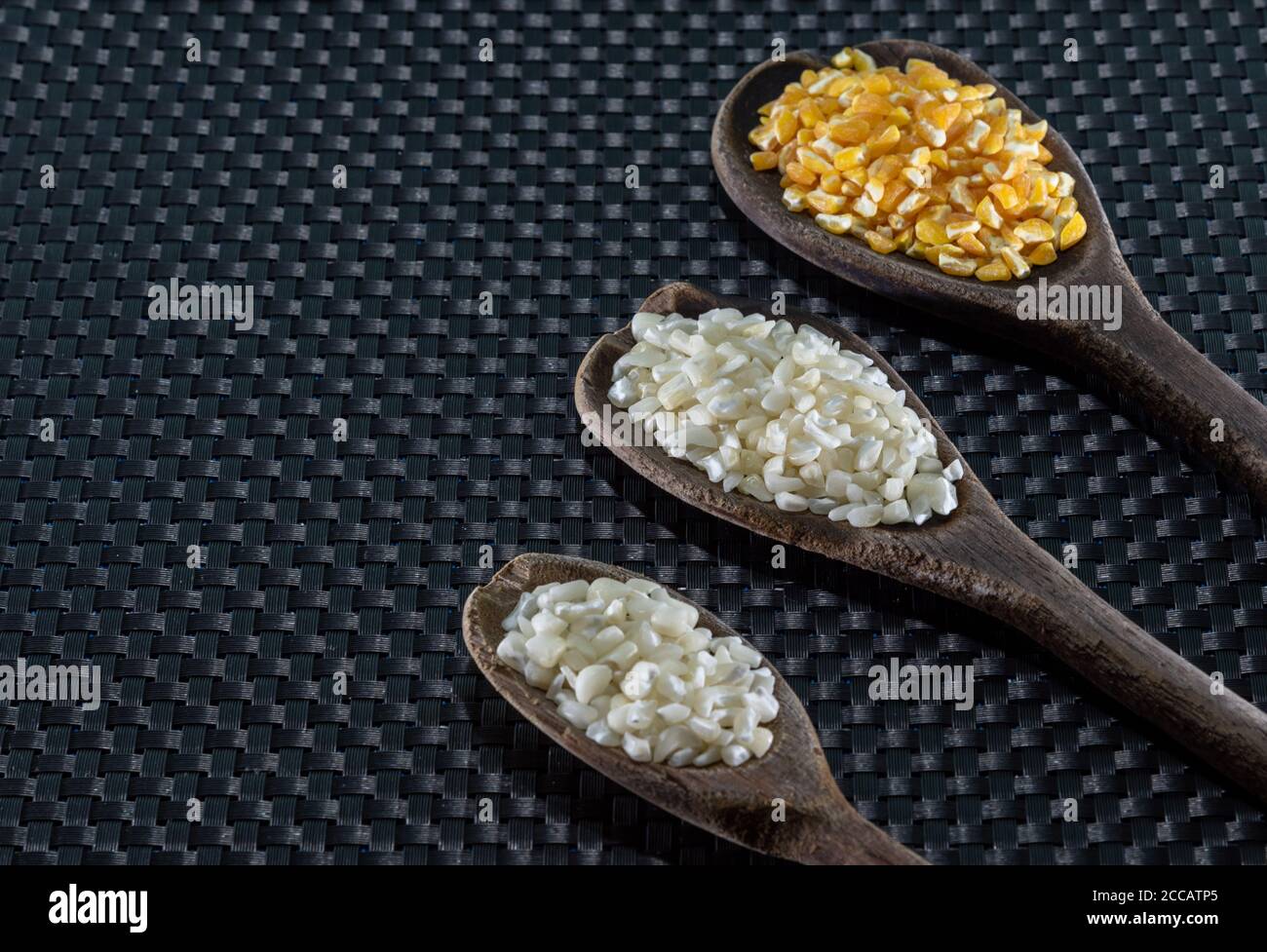 Corn seeds for hominy preparation. Hominy in yellow and white in wooden spoons. Brazilian