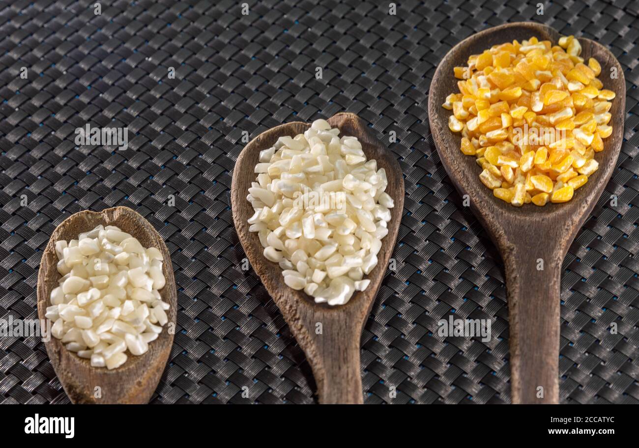 Corn seeds for hominy preparation. Hominy in yellow and white in wooden spoons. Brazilian