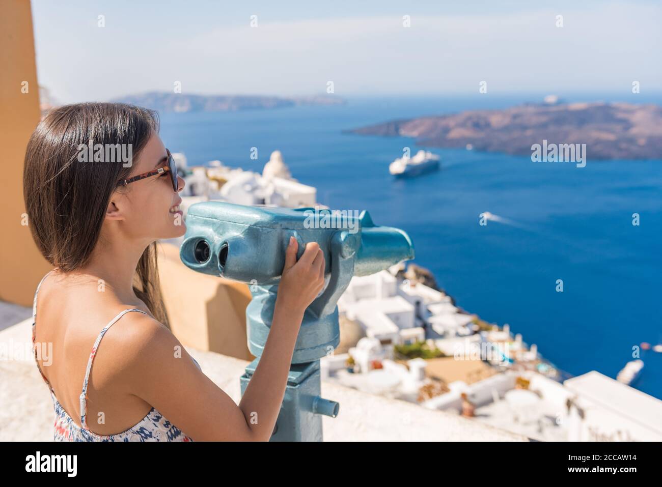 Travel tourist on Europe holiday walking in Santorini city street looking through tower viewers coin machine, binoculars to watch cruise ships in Stock Photo