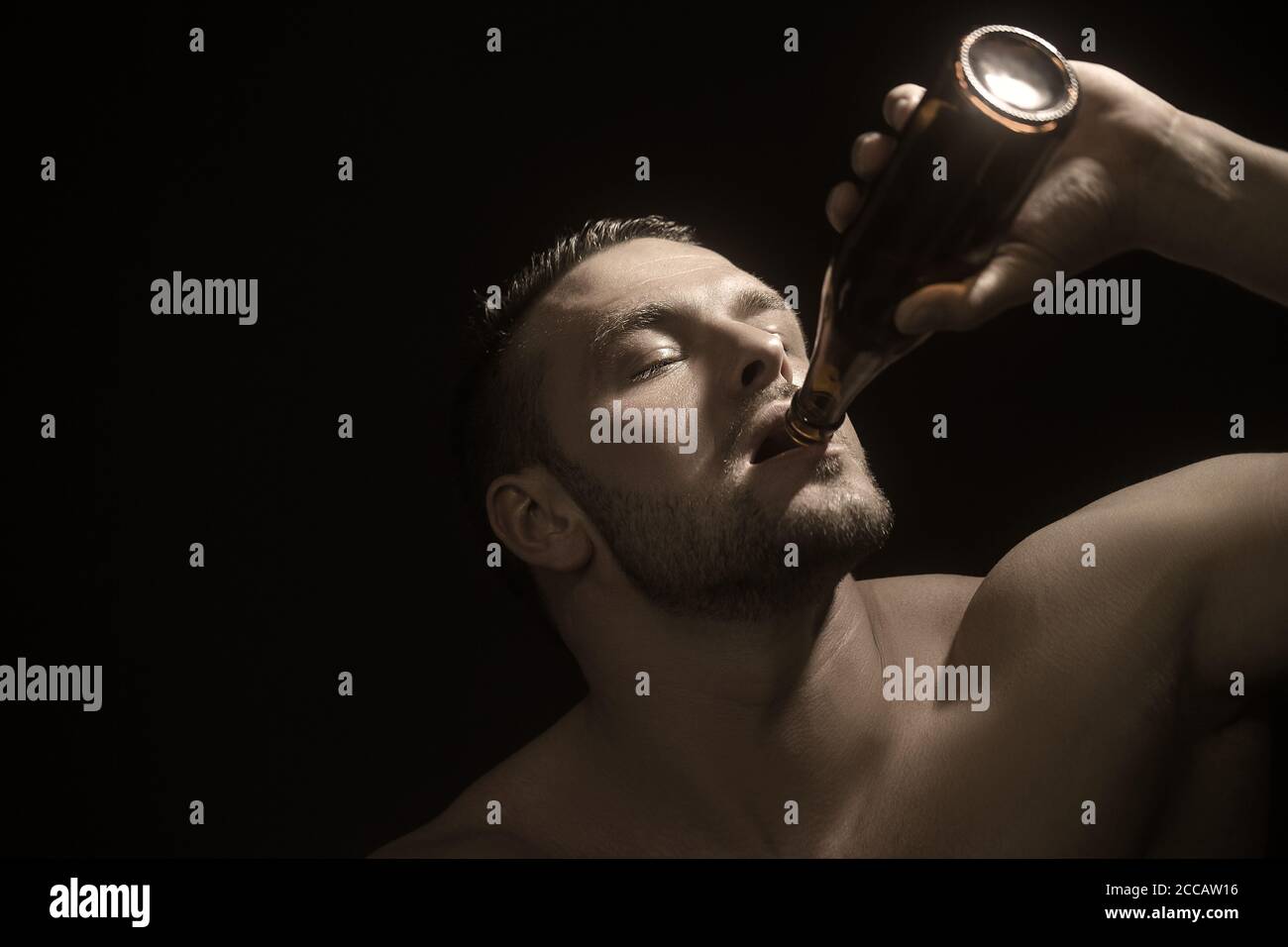 Stylish muscular guy enjoys the taste of craft beer. Studio photo against a dark background. Stock Photo