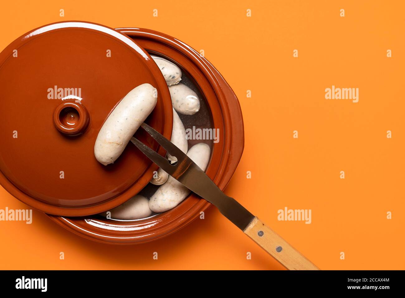 Boiled weisswurst, german white sausage cooked in a ceramic pot, on orange background. Top view of bavarian veal sausage. Germany national food. Stock Photo