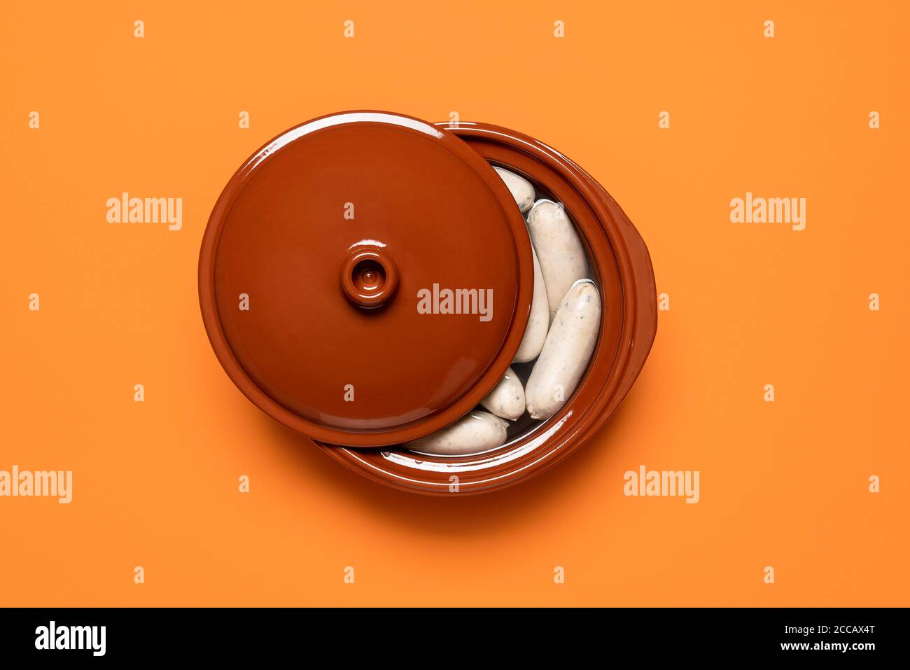 Boiled white sausage in a brown pot, isolated on orange background. Top view of Bavarian veal sausage in water. German traditional weisswurst. Stock Photo