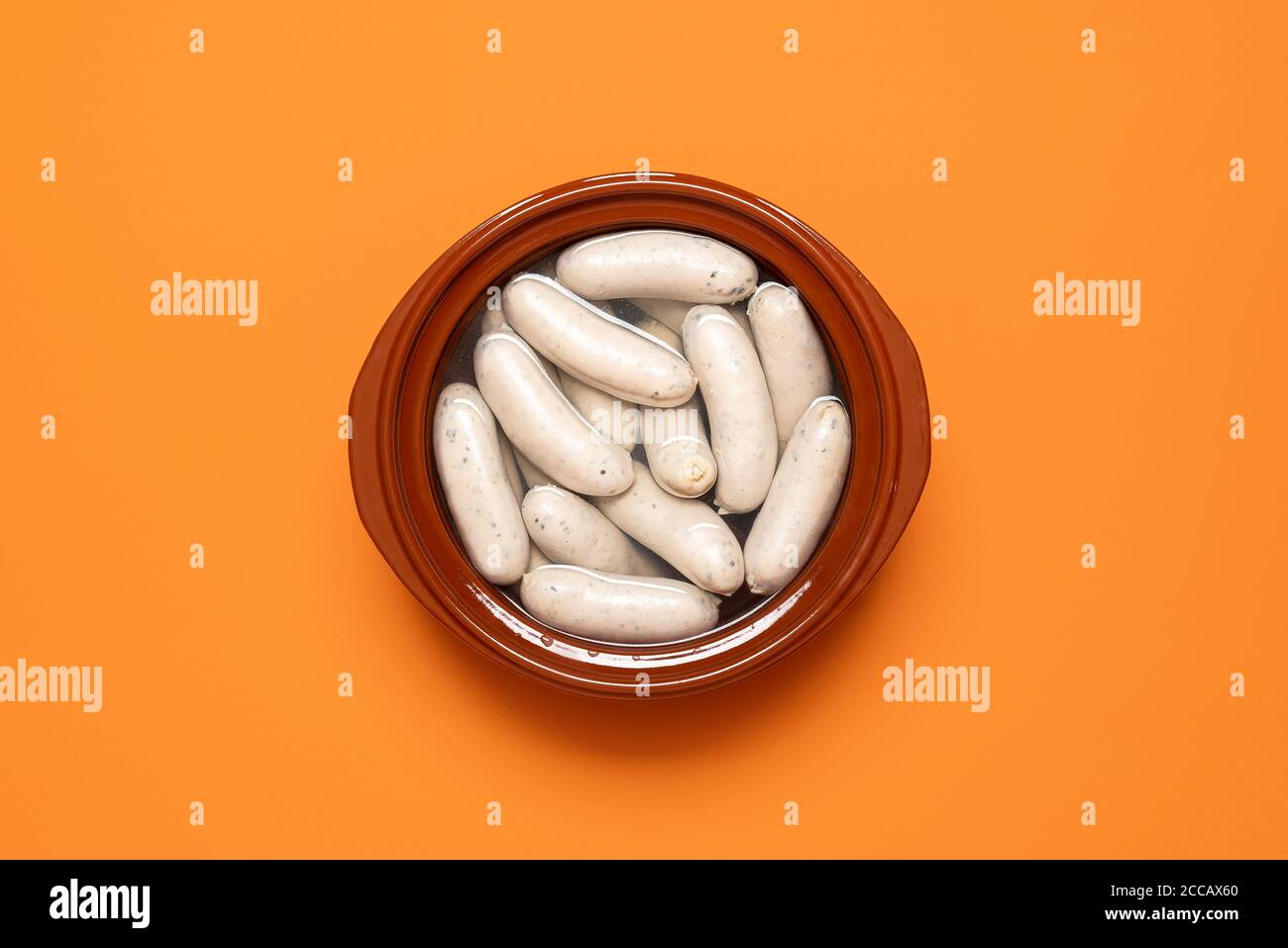 German white sausage boiled in a brown pot, isolated on orange background. Top view of weisswurst, bavarian veal sausage. Oktoberfest traditional food Stock Photo