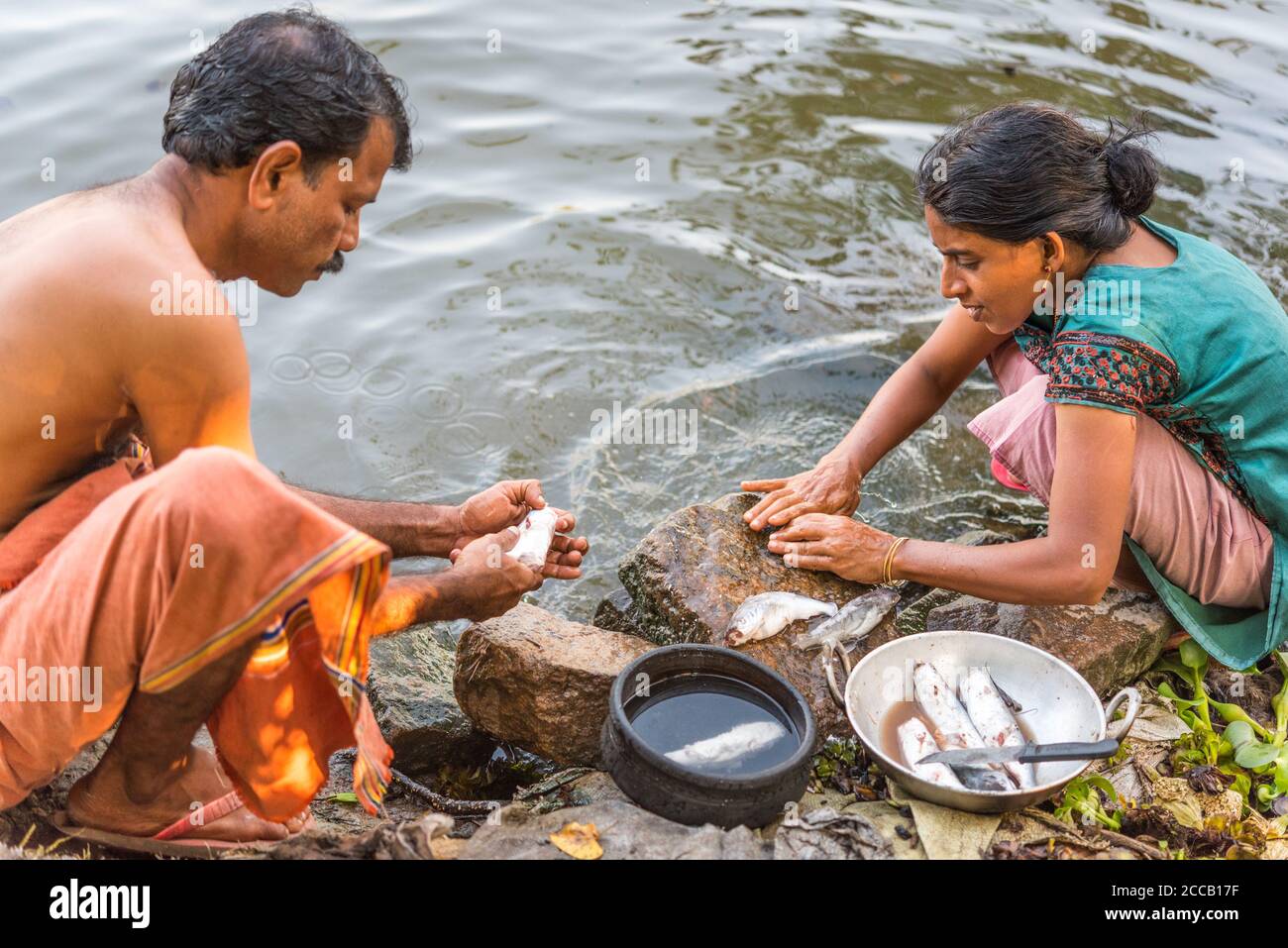 Alappuzha, Kerala, India - December 23, 2015: Keralan man and woman clean fish on the shore of the Pamba River (a part of the Backwaters). Stock Photo