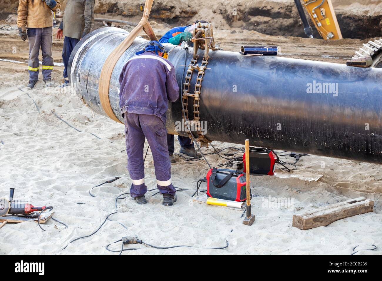 Welder workers  welding big pipes and wearing protective clothing and safety gear. Stock Photo