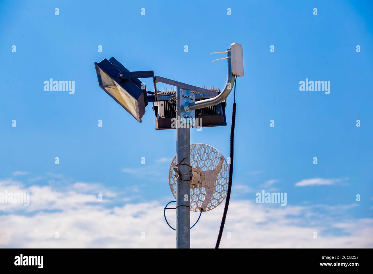 Wifi antenna on a metal light pole outdoors with blue sky background. Stock Photo
