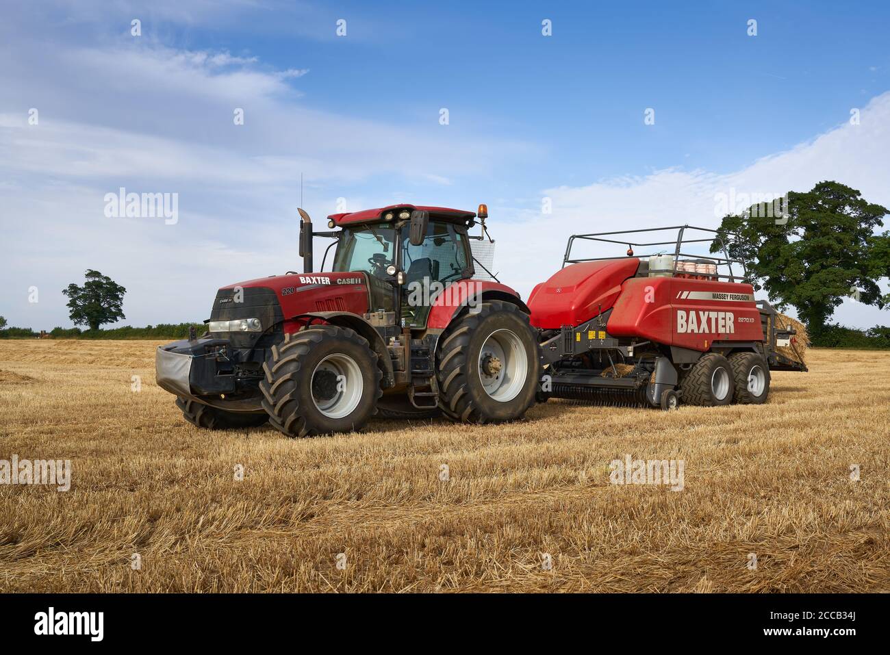 Case Puma 220 tractor baling in a Lincolnshire field with a large Massey Ferguson 2270XD baler on an August summer evening Stock Photo