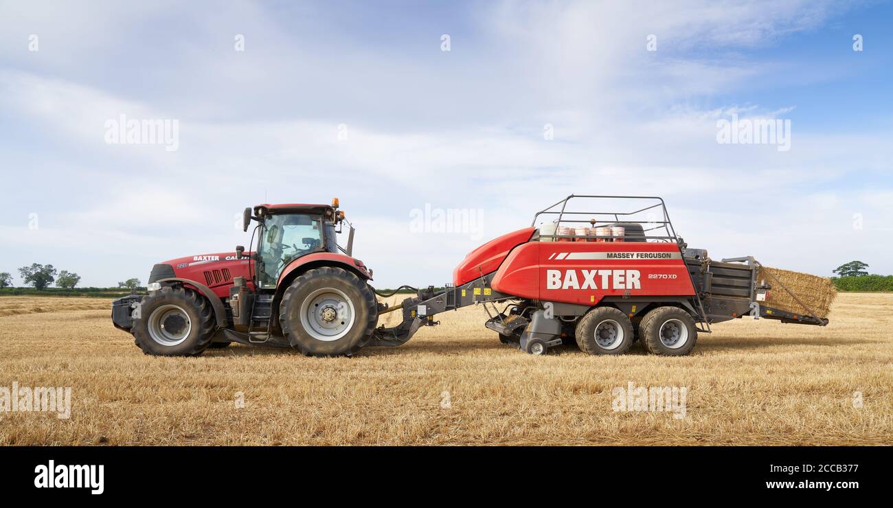 Case Puma 220 tractor baling in a Lincolnshire field with a large Massey Ferguson 2270XD baler on an August summer evening Stock Photo