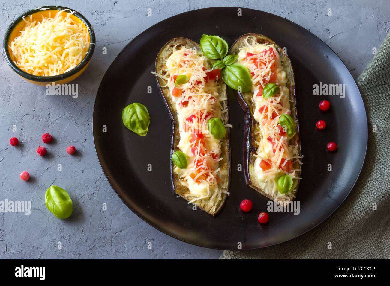 Eggplant stuffed with tomatoes, grated cheese and cranberries, garnished with Basil on a dark plate over gray slate Stock Photo